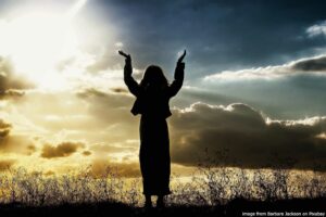 Silhouette of a woman raising her hands to the sky in front of a sunset